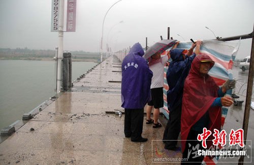 图为大风吹垮的桥栏已被清理，工人们在冒雨加装围挡。